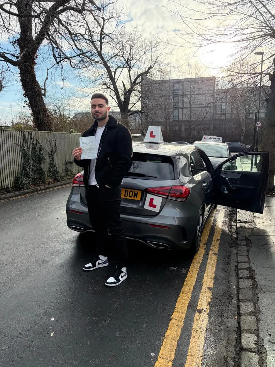 New driver holding his pass certificate beside a grey Mercedes A-Class driving school car with L-plates