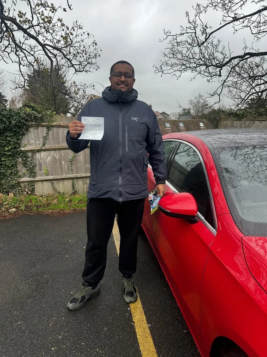 Learner in a navy jacket holding his driving test pass certificate beside a red Mercedes tuition car