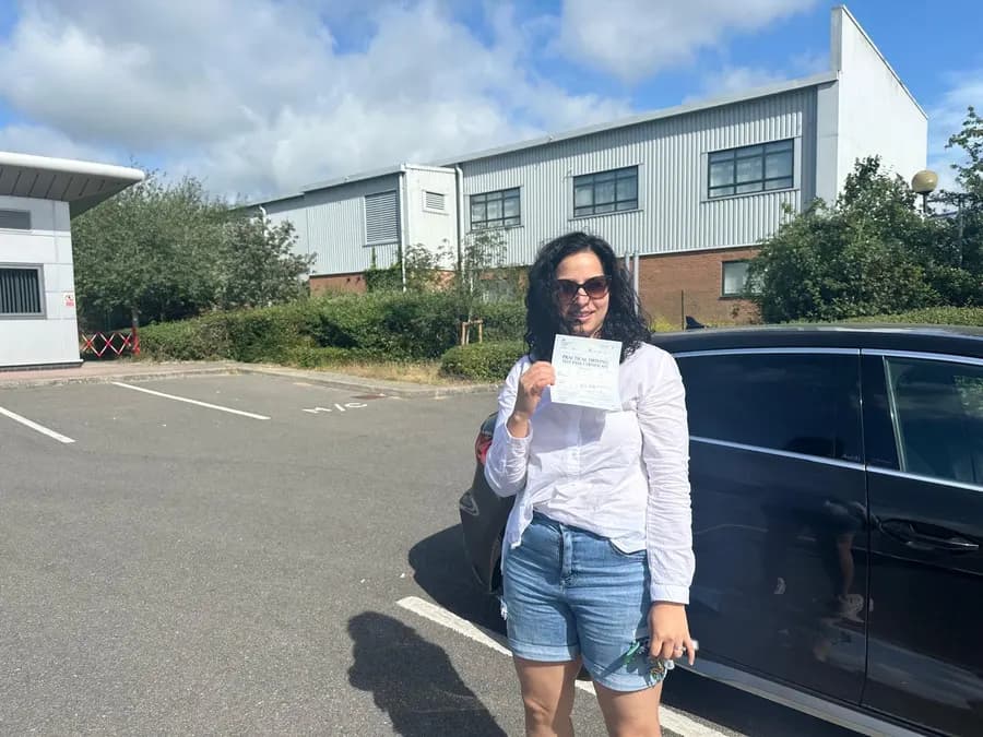 Smiling woman holding her driving test pass certificate beside a black car straight after her test