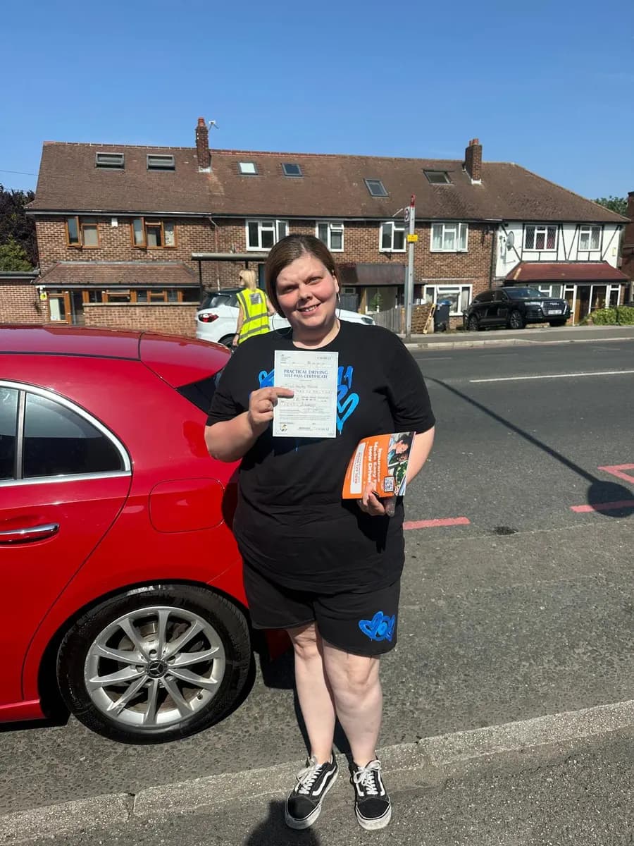 Delighted student holding her driving test pass certificate next to a red tuition car on a sunny day