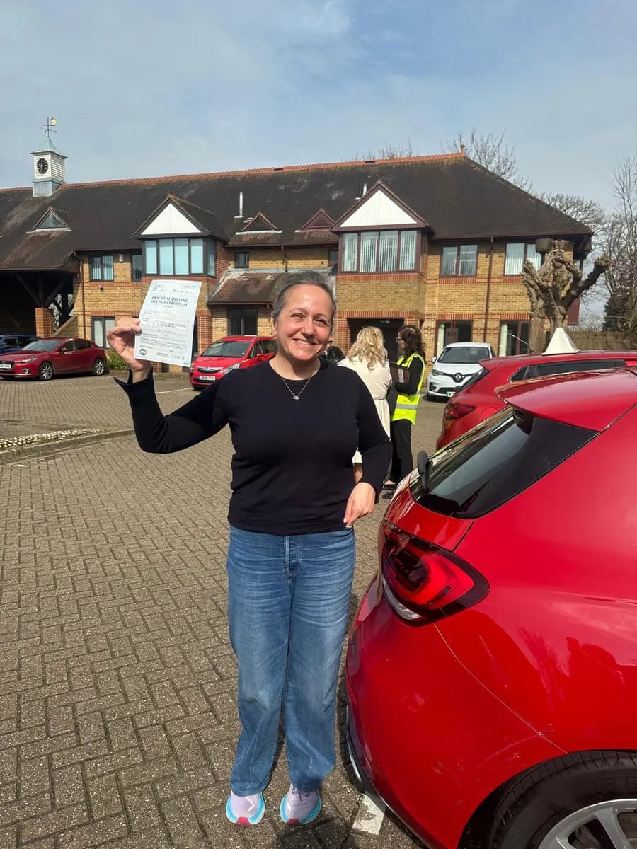 Learner driver raising her pass certificate in celebration beside a red tuition car