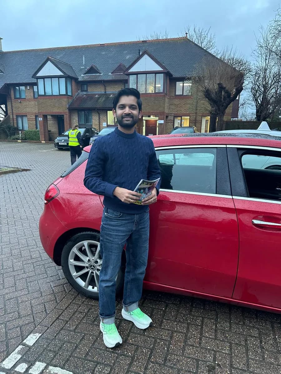 Student in a navy jumper holding his pass certificate next to a red hatchback tuition car